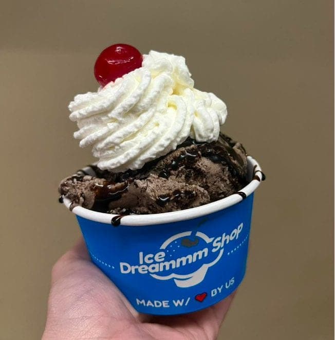 Ice cream cup piled with chocolate pieces, whipped cream, and a cherry