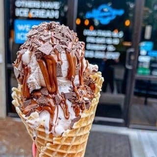 Waffle cone of ice cream topped with chocolate shavings and caramel and chocolate drizzle