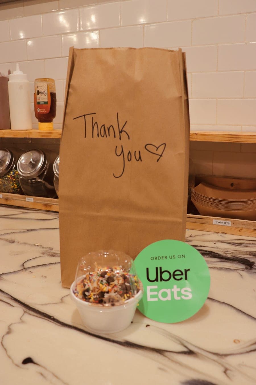 Takeout bag marked "Thank you" beside a cup of ice cream and an Uber Eats sticker