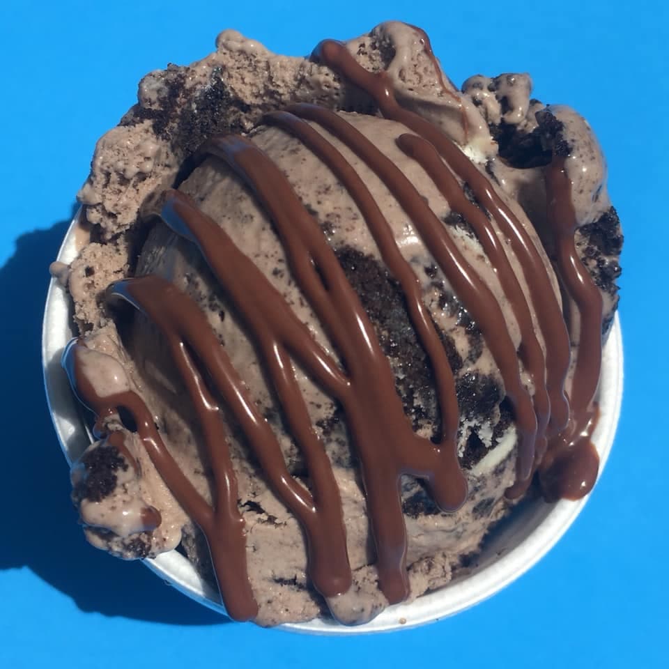 Scoop of homemade ice cream with cookie pieces and a chocolate drizzle in a cup